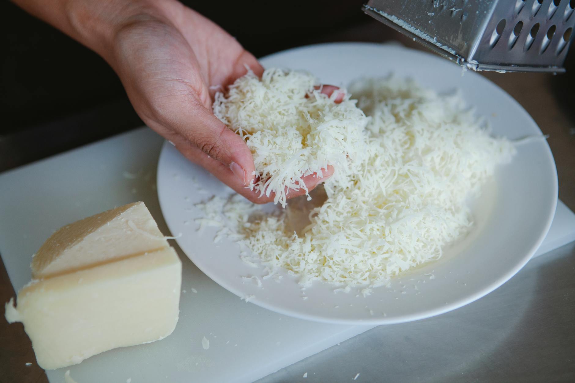 Jak zrobić domowy twaróg krok po kroku – praktyczny poradnik dla początkujących Dłoń ścierająca świeży ser na talerz w domowej kuchni
