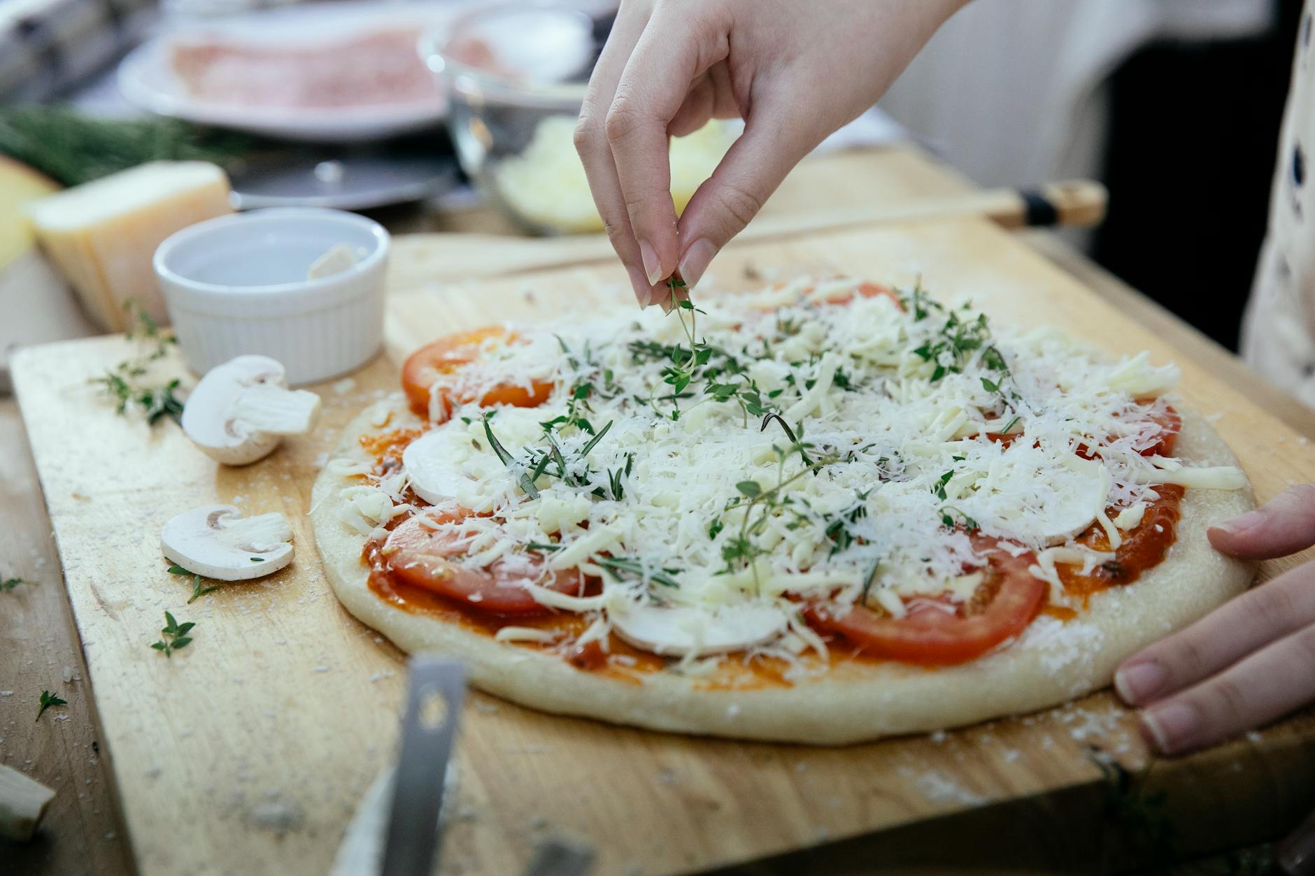 Kobieta posypuje świeżymi ziołami surową pizzę z serem i warzywami