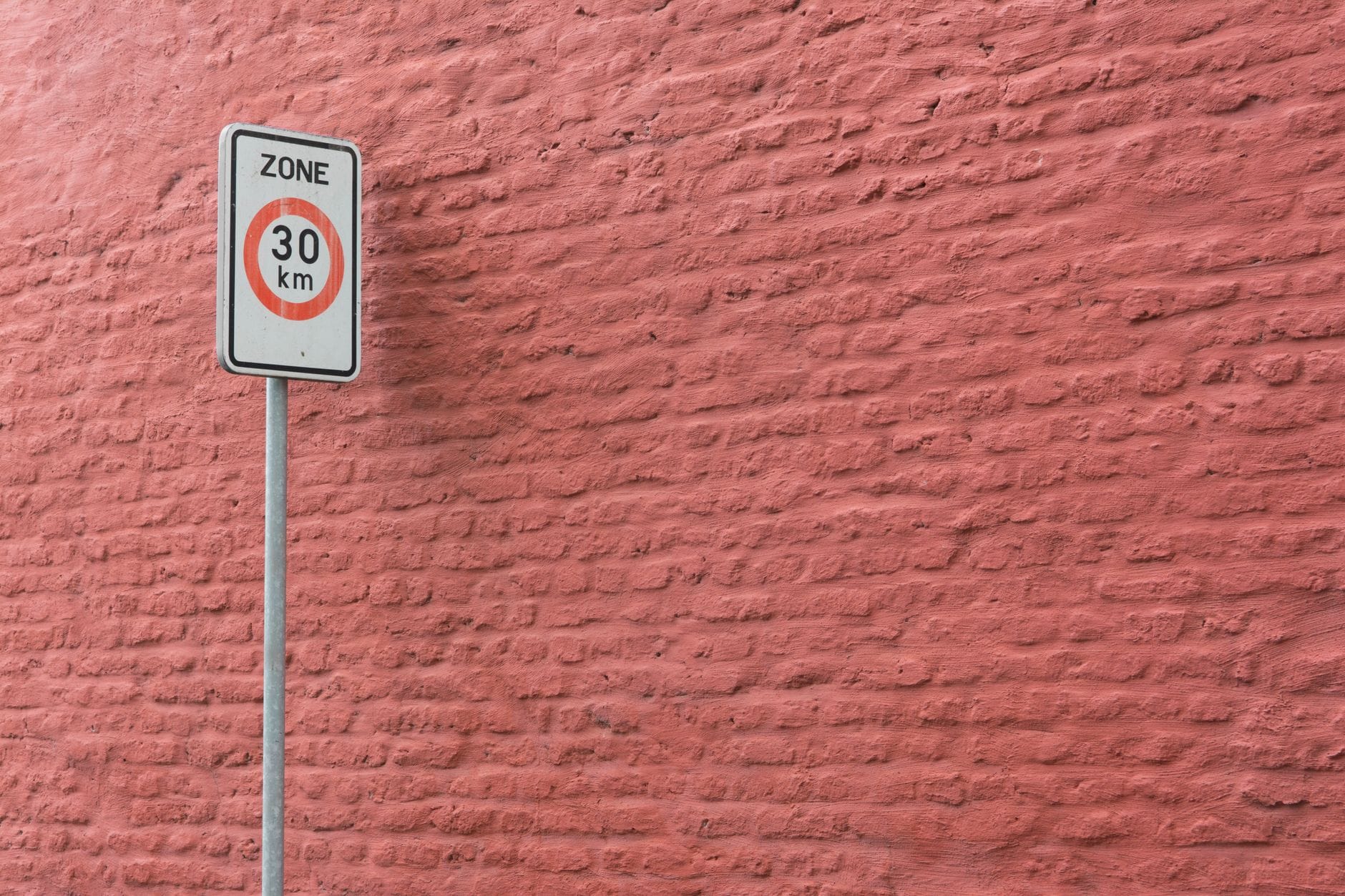 Znak ograniczenia prędkości do 30 km/h na różowym ceglanym murze